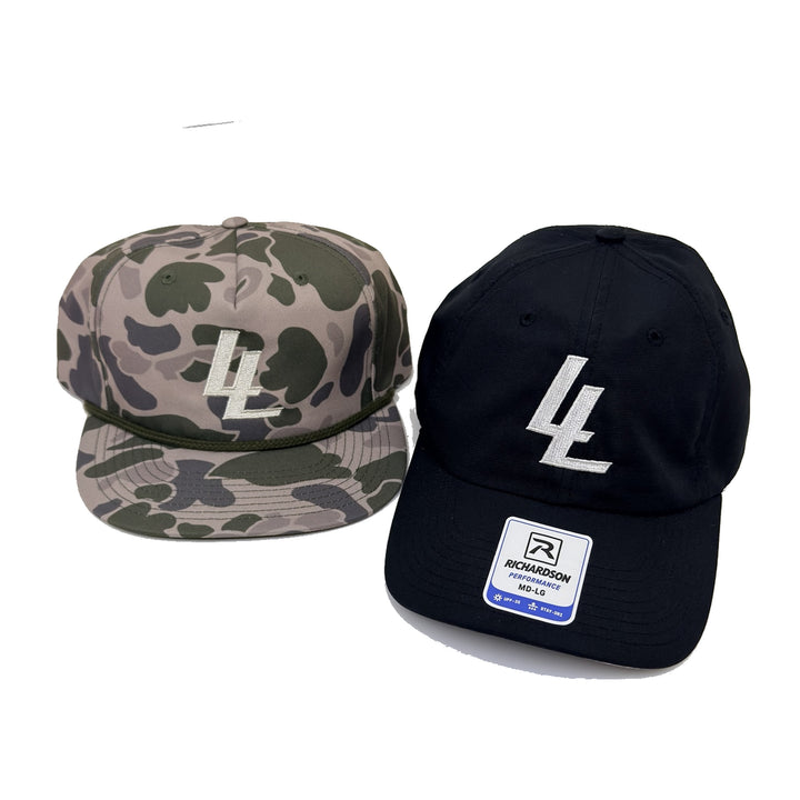 Translation missing: en.Two flat-brim baseball caps on a white background: one in green, beige, and gray camouflage with a cream embroidered LL llogo, and one solid black with a white embroidered 'LL' logo and a visible Richardson  label