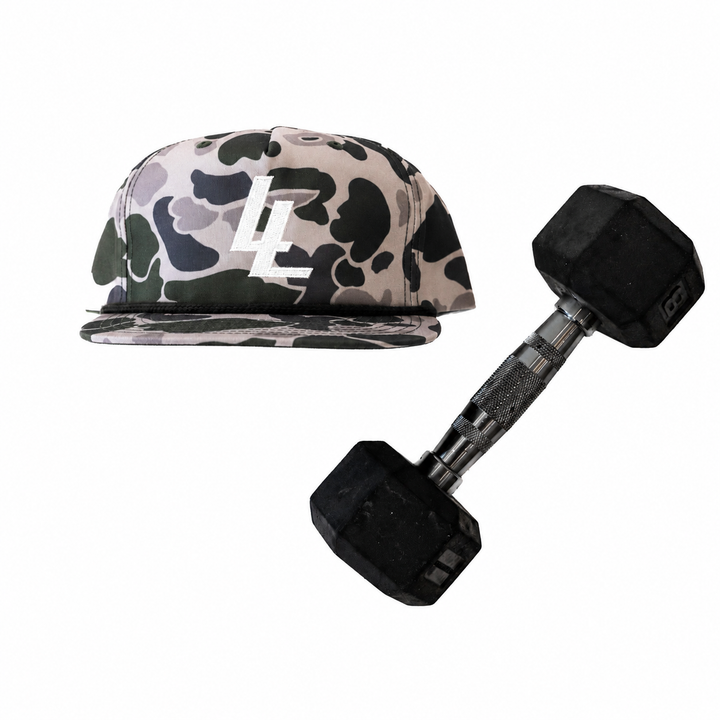 Translation missing: en.A camouflage baseball cap with a Cream embroidered LL logo on the front, shown next to a black hex dumbbell on a plain white background