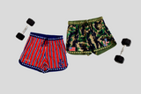 Two pairs of shorts, one red and white striped with an American flag logo, the other camouflage, along with two dumbbells on a light gray background.