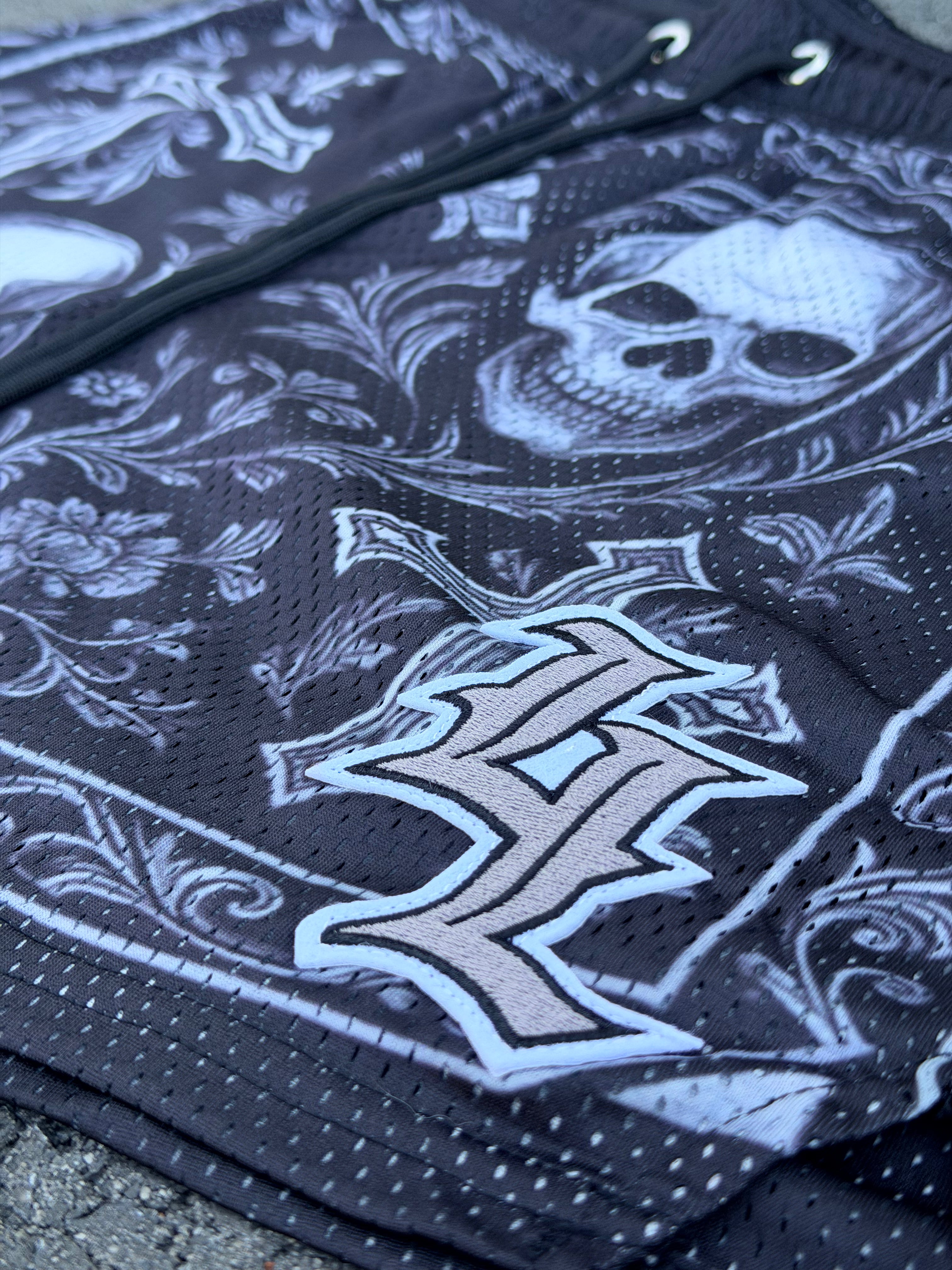 Close up of gothic LL logo on skull and cross mesh gym shorts