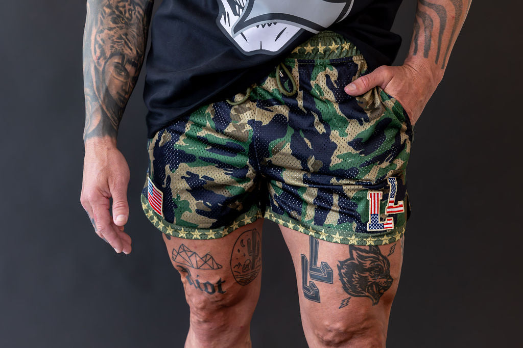 Person wearing camouflage shorts with American flag patches on a dark background