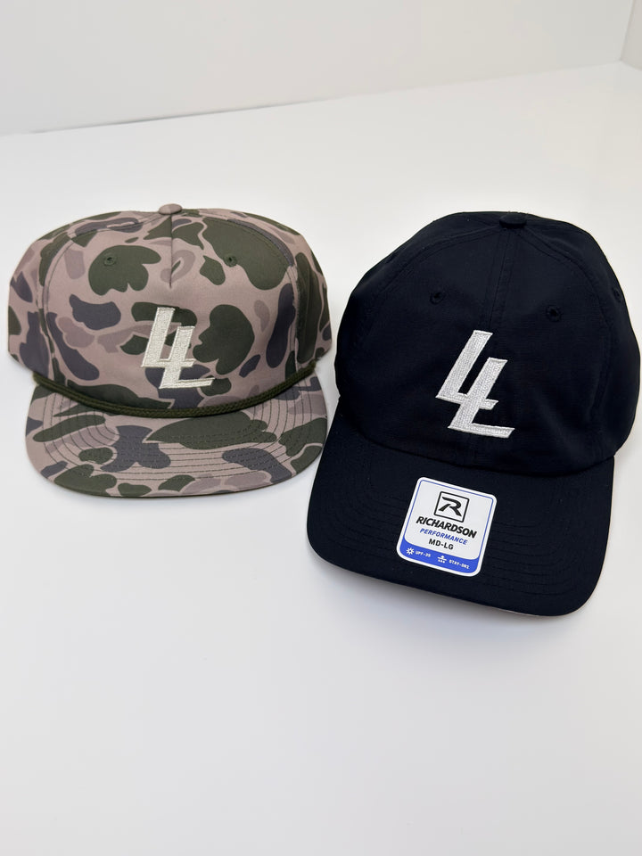 Translation missing: en.Two flat-brim baseball caps on a white surface: one in beige and green camouflage with a cream embroidered LL logo, and one black with a white stylized 'LL' logo and a visible Richardson brand patch on the brim