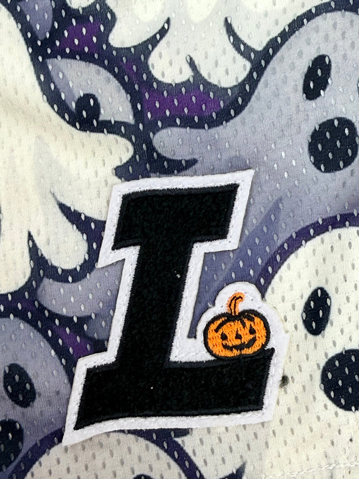 Translation missing: en.Close-up of a black embroidered letter L patch with a small orange pumpkin accent, placed on a white mesh fabric with a ghost pattern