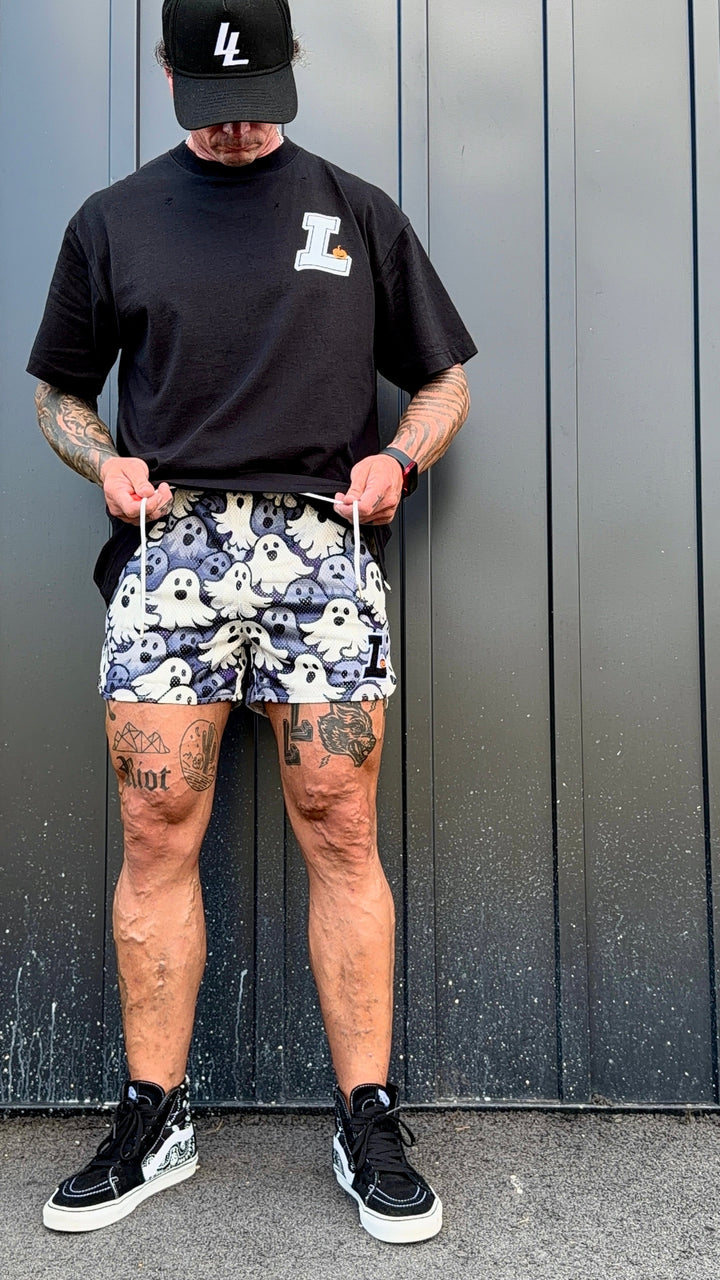 Translation missing: en.A man wearing a black t-shirt, a black baseball cap, and a pair of black-and-white ghost-print shorts, standing in front of a dark gray corrugated metal wall