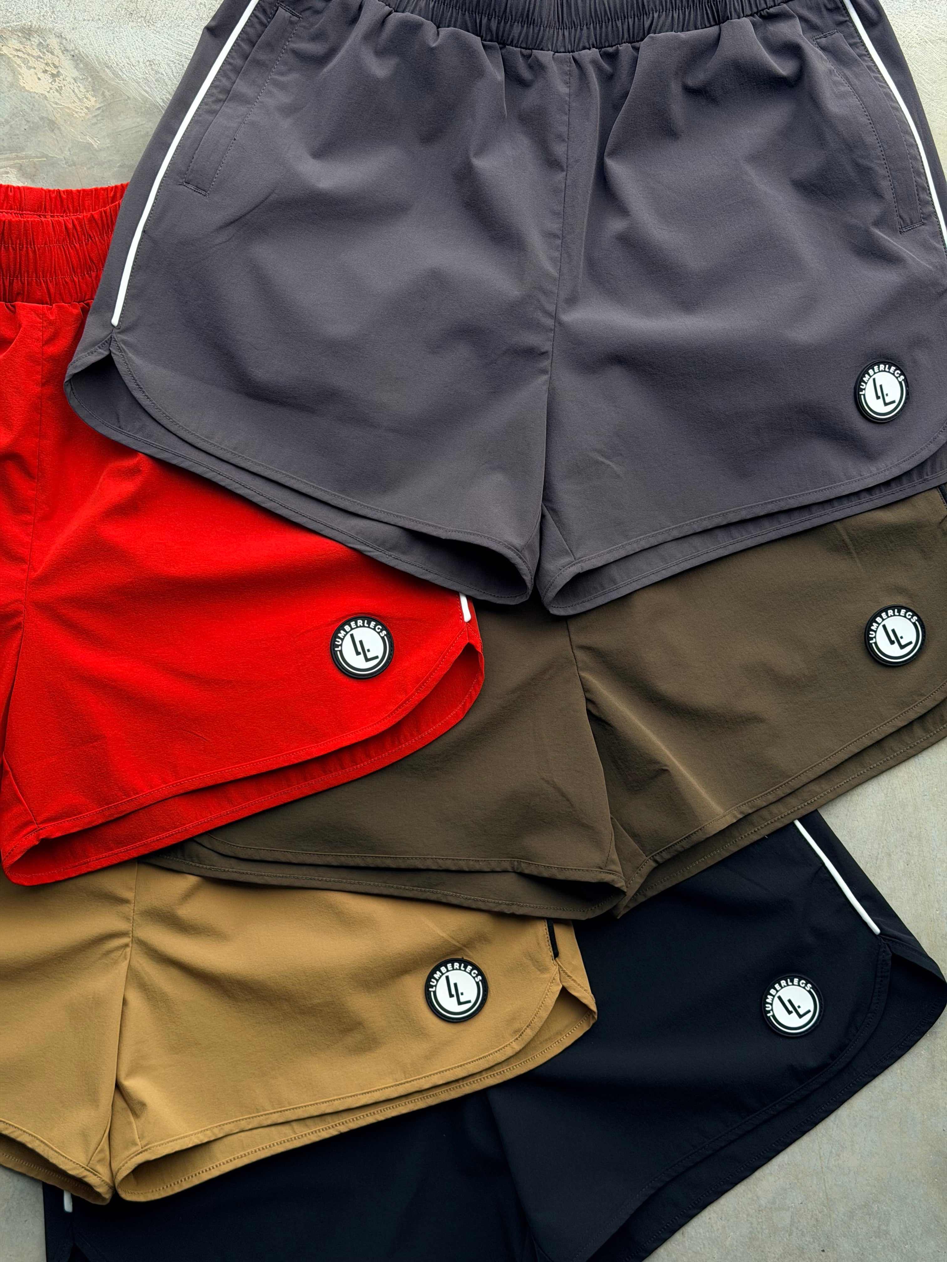 Five color ways of the OG 3” inseam shorts. Obsidian Black, Mocha Tan, Tactical Thigh Green (army dark green), Red Riot (RED), Dark Grey (Gray)